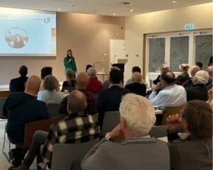 Wethouder presenteert tijdens het Ontzorgingsprogramma van de Gemeente Dordrecht, met publiek in de zaal.